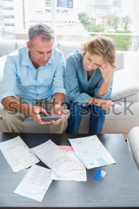 middle-aged-couple-sitting-on-their-couch-paying-their-bills-at-home-in-the-living-room